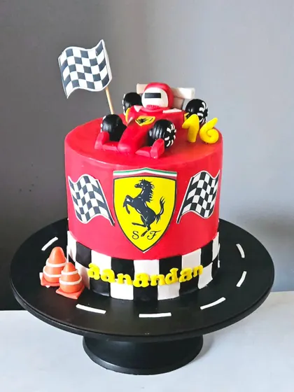 A sleek Ferrari-themed cake for a racing fan. This cake is covered in red-colored ganache and features the iconic Ferrari logo, a checkered flag pattern, and a handcrafted Formula 1 car topper.