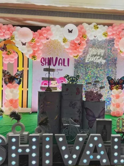 A large-scale butterfly-themed first birthday party. The stage includes multiple backdrops, a shimmer wall, and a white picket fence.