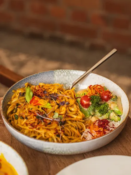 A bowl of savory noodles and fresh salad, shot on a wooden surface. The image has a warm, inviting feel that emphasizes the freshness of the ingredients.