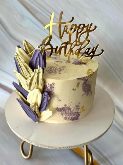 A striking birthday cake with abstract, sculpted chocolate shards in shades of lilac and white. The design is finished with a modern palette knife texture and flecks of gold leaf.