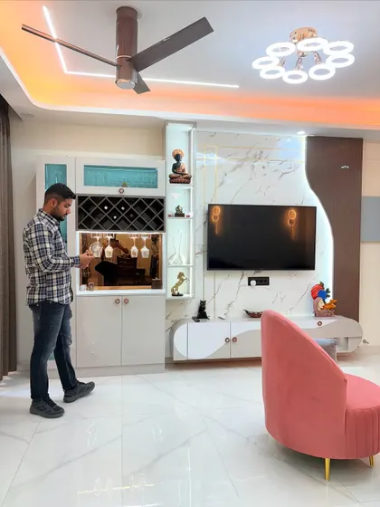 This wide shot captures the full living area, showing how the TV unit, bar cabinet, and modern furniture come together. The color scheme of white, grey, and pink creates a sophisticated yet comfortable atmosphere.