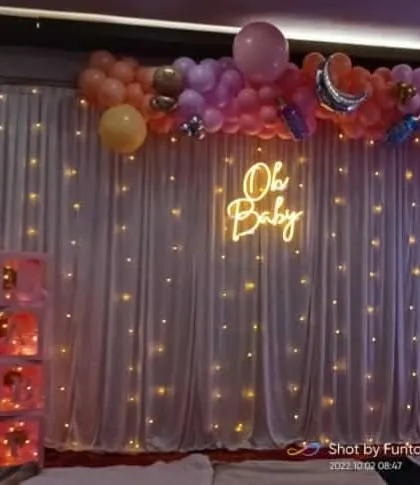 This 'Oh Baby' theme with a neon sign, balloon arch, and fairy lights is a great option for a modern and chic baby shower.