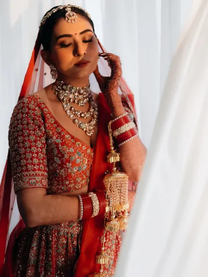 A dramatic bridal portrait using natural window light. The play of light and shadow beautifully highlights her features and the richness of her red lehenga.
