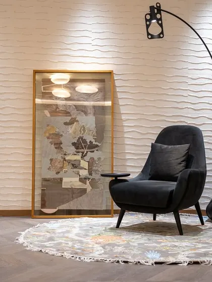 A cozy reading nook within a Gurgaon apartment bedroom. The space is defined by a custom black armchair with an integrated side table, set against a hand-crafted textured wallpaper. This corner is designed as an inviting spot to pause and rest.