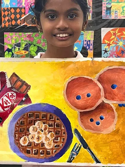 A proud student shows off her completed food painting. Her use of bright, cheerful colors and confident brushwork brings the scene to life.