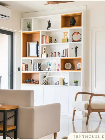 A custom-designed bookshelf serves as both storage and a display for the client's personal items and awards. The asymmetrical design with wood-accented boxes adds a dynamic and modern touch to the living area.