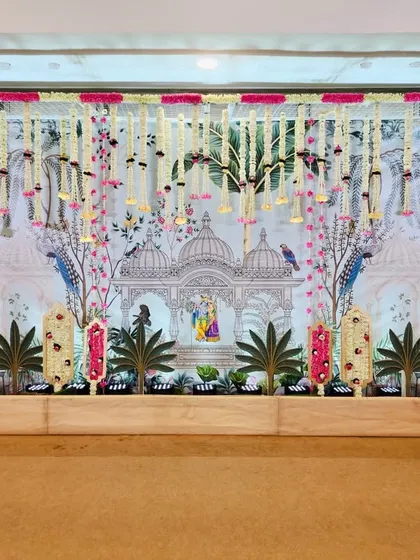 We designed this elaborate stage for a baby shower with a Vrundavan theme. The backdrop features a custom print of a temple scene with peacocks, accented by hanging floral strings in pink and white for a soft, celebratory feel.