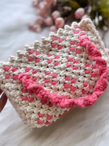 This design features a unique pattern where the pink cord is woven into the off-white body to create a dotted effect. The handle is a sturdy, twisted macrame braid.