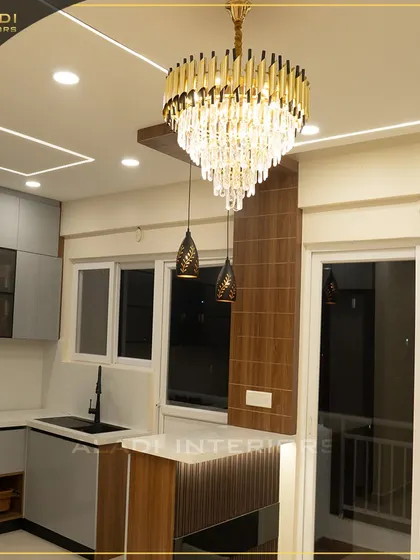 A beautiful kitchen view highlighting a magnificent crystal chandelier. The design combines modern grey cabinets with a wooden breakfast bar and elegant pendant lights.