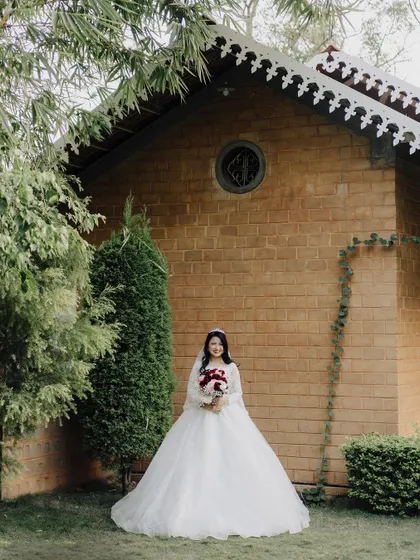The elegance of a Christian wedding is captured in this full-length portrait of the bride in her beautiful white gown, standing before a rustic brick building.