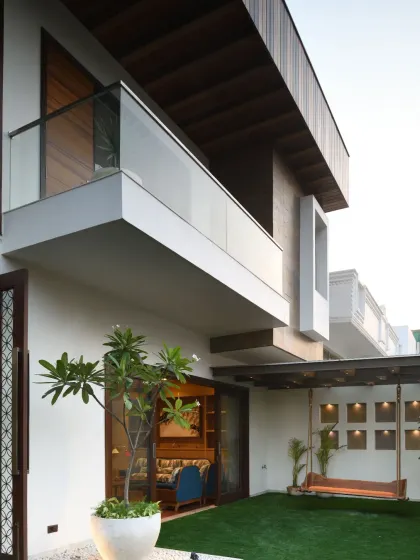 The ground floor garden of the Ashraya Residence is a tranquil retreat with lush potted plants and cozy outdoor furniture. The upper floors overlook this green haven, fostering a seamless visual and spatial connection throughout the house.