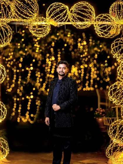 A full-length portrait of the groom, looking sharp and confident against the festive lights.