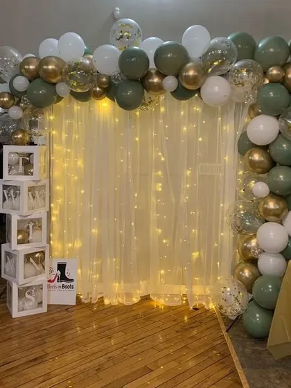 A simple yet elegant backdrop with an olive green and gold balloon arch, fairy light curtain, and 'love' blocks for a baby shower or anniversary.
