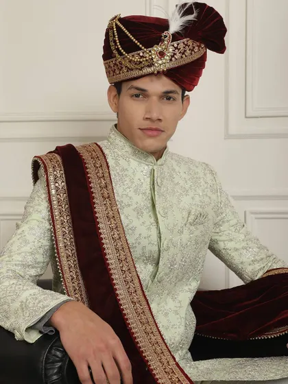 A regal look featuring a mint green sherwani paired with a deep maroon velvet stole and a matching embellished turban.