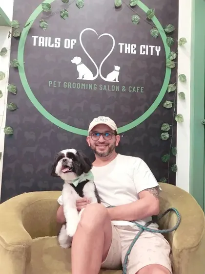 This proud pet parent is all smiles with his handsome dog after a visit to our salon. Our logo wall is a popular spot for post-grooming photos!