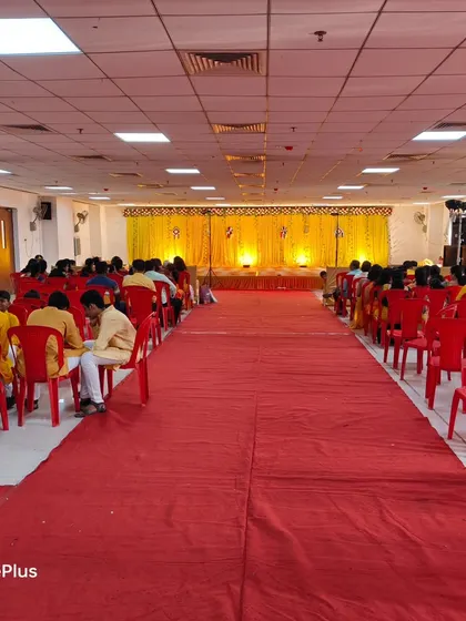The seating arrangement for a Haldi ceremony in a hall. The red carpet and chairs are set up facing the bright yellow stage.