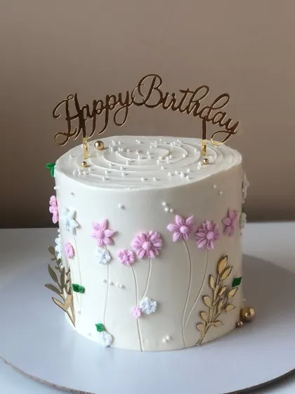 A white cake with a field of delicate pink wildflowers and golden leaves.