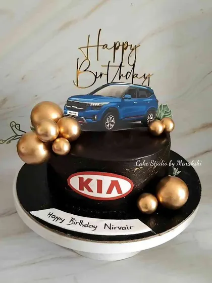 A KIA car themed cake for a birthday celebration. This design features a picture of the car, the KIA logo, and elegant gold spheres.