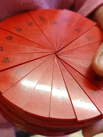 A child holds a complete set of Montessori fraction circles. These beautiful, hands-on materials allow children to explore the relationships between parts and the whole in a tactile, intuitive way.
