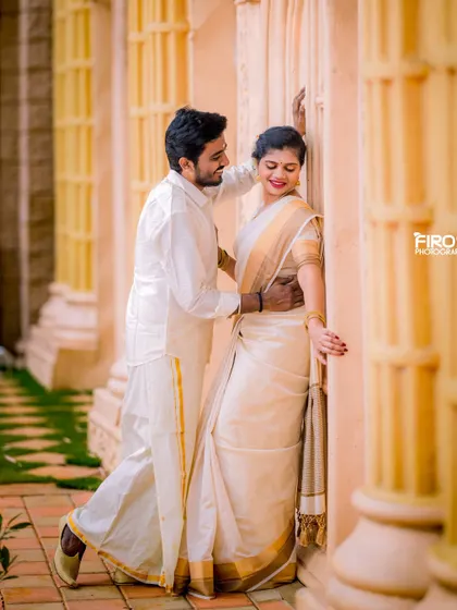 A romantic and slightly playful moment in a sunlit corridor. The couple's classic white and gold attire glows in the warm light.