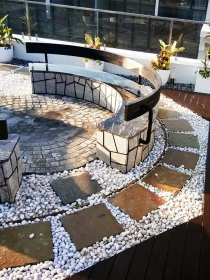 This terrace at Embassy Boulevard features a stunning custom-built curved seater made from natural stone. Set on a bed of white pebbles and a wooden deck, it serves as a sculptural and functional centerpiece.
