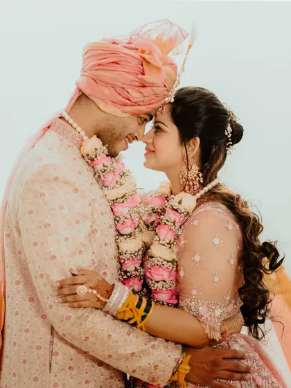 An intimate forehead-to-forehead pose, capturing the deep connection between the bride and groom. The soft pastel colors of their outfits and the floral garlands add to the romance.