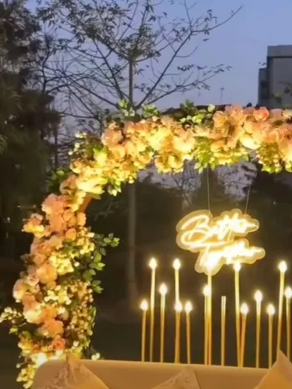 An outdoor photo corner for an engagement party, featuring a semi-circular floral arch, candle-like LED lights, and a "Better Together" neon sign.