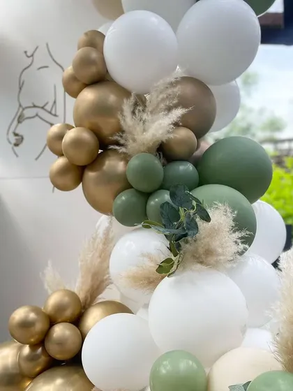 A close-up of the balloon garland from the minimalist baby shower, showing the mix of sage, gold, and white balloons with pampas grass.