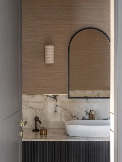 Another view of the powder room, highlighting the elegant arched mirror and ceramic wall sconce. The design proves that even the smallest rooms can be packed with style and personality.