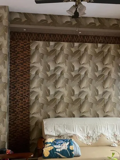 A living room with a combination of wallpapers. The main wall features a large leaf pattern, which is complemented by a textured tile pattern on the pillar, creating a unique and layered look.