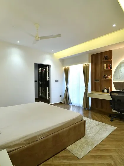 This contemporary bedroom features a stylish and functional workspace integrated into the room's design. The herringbone wood flooring, fluted wood paneling, and large backlit mirror create a space that is warm, modern, and perfect for both rest and productivity.
