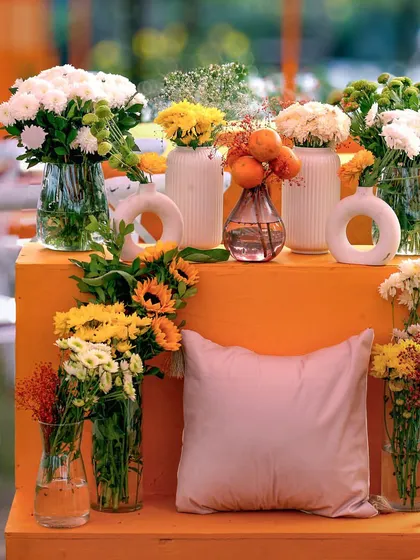 A close-up of the floral decor for the 'Love in Mexico' theme, featuring bright yellow and white flowers in minimalist vases on a bold orange stand.