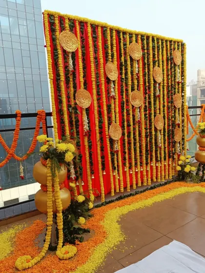 A rooftop Haldi decor setup. I used a backdrop of red fabric and marigold strings, with a floor rangoli and traditional pots, to transform an urban space into a traditional celebration venue.