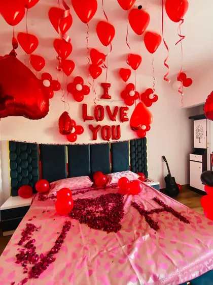 A personalized romantic setup with the couple's initials "V" and "H" written in rose petals on the bed.