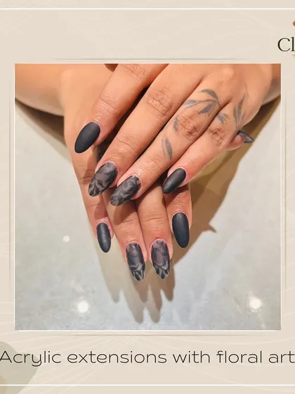 Dark and romantic. These almond-shaped acrylic extensions feature a matte black finish with subtle, hand-painted floral art, creating a moody and sophisticated design.