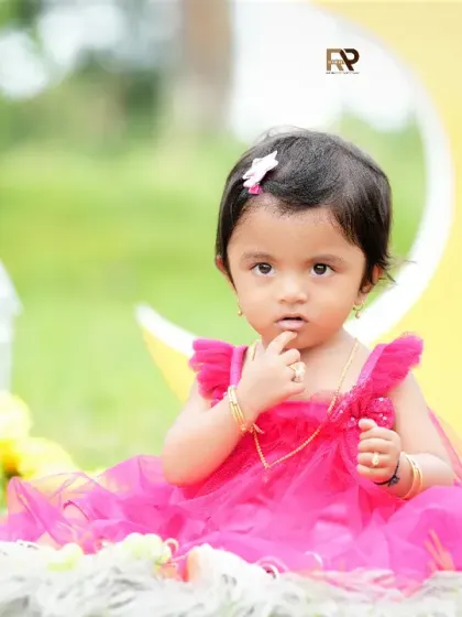 An outdoor portrait of a baby girl in a pink dress, sitting on a fur rug with a crescent moon prop. The natural setting adds a beautiful and serene quality to this dreamy photo.