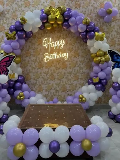 An elegant butterfly-themed ring backdrop using purple, white, and gold balloons, with a neon sign and 3D butterfly accents.