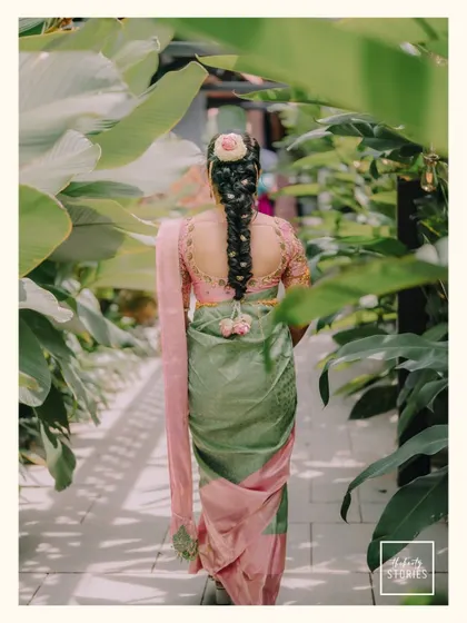 A beautiful shot of the bride from behind, showcasing her intricate hairstyle adorned with flowers and the elegant drape of her green and pink saree.
