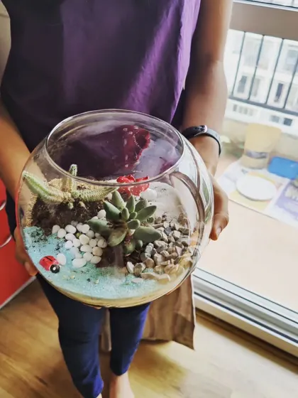 A close-up of a finished terrarium, showcasing the layers of sand, soil, and carefully placed succulents and figurines. It's a tiny world in a bowl.