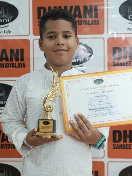 A young student in traditional kurta proudly holds his award for musical excellence.