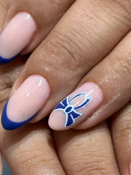 A close-up of a hand-painted blue bow on an accent nail, part of a chic and modern French manicure set.