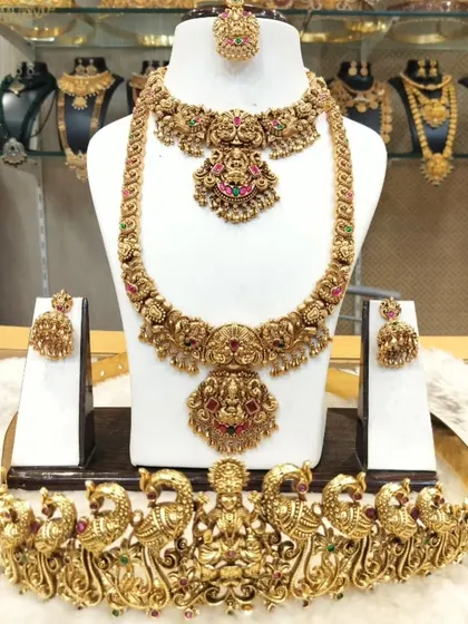 An antique gold-finish bridal set featuring a Lakshmi choker, a matching haram, and a grand peacock vaddanam.