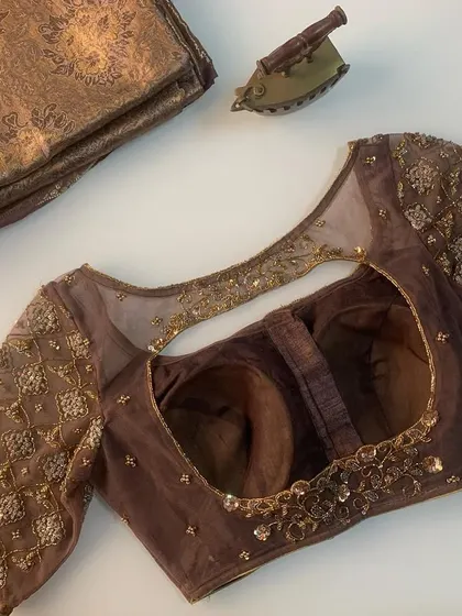 A unique brown blouse with sheer sleeves and a large back cutout. The blouse is laid flat with a matching brocade fabric piece.