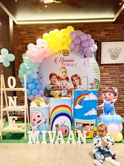 This Cocomelon first birthday decor is perfect for an indoor venue with a rustic feel. The brick wall complements the wooden props and colorful balloons, and the birthday boy seems to approve.