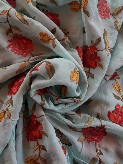 A sky-blue organza with vibrant red and yellow floral embroidery. The contrast of colors makes this fabric a bold and beautiful choice for festive wear.