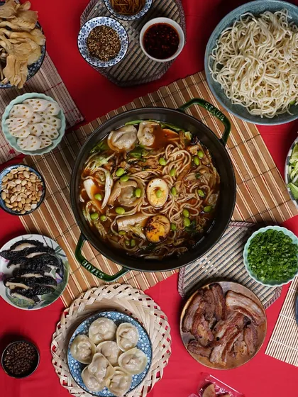 A beautiful flat lay of the Hot Pot experience. You can see the central pot surrounded by all the delicious components: noodles, dumplings, sliced pork, eggs, and fresh vegetables, showcasing the abundance of the kit.