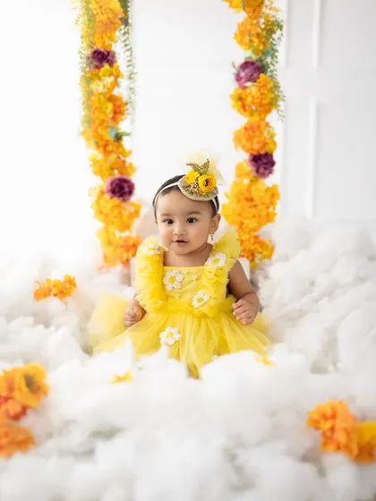 A magical first birthday photo with the birthday girl sitting amidst fluffy clouds and a floral swing, looking like a little angel.