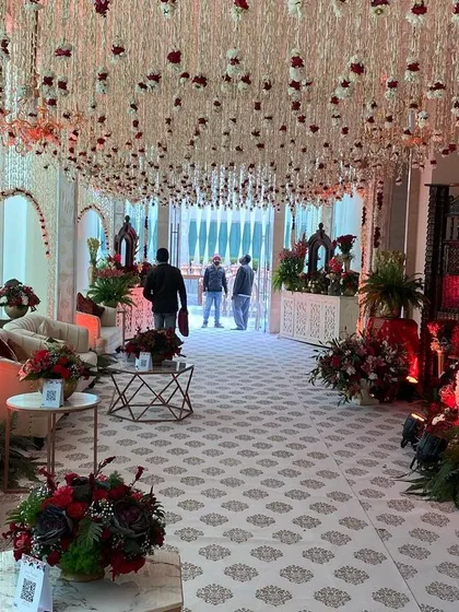 A comfortable and elegant lounge area for guests at a traditional wedding. The space is decorated in a classic red and cream palette, with a ceiling of cascading floral strings that adds a touch of delicate beauty.