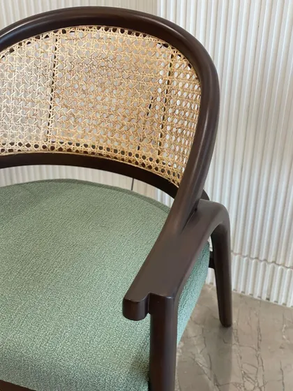 A close-up of our classic dining chair, highlighting the beautiful contrast between the dark wood frame, the natural hand-woven cane back, and the soft green bouclé seat.