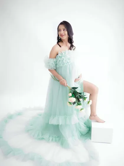 A playful and lighthearted portrait. The mom-to-be, in a flowing mint green gown, holds a bouquet of white flowers, her pose full of joy and energy.